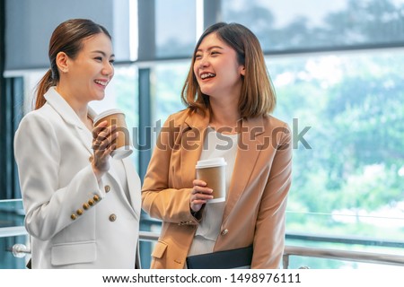 Two asian businesswomen talking during coffee break in modern office or coworking space, coffee break, relaxing and talking after working time, business and people partnership concept