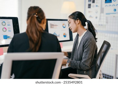 Two asian businesswomen are working together in the office. They are looking at charts and graphs on a computer screen, analyzing financial data - Powered by Shutterstock