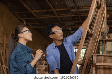 Two Asian Carpenters In A Construction Workshop. Business Man And Woman Working Together Woodwork