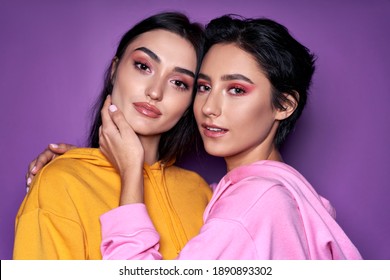 Two Asian And Caucasian Girls Lesbian Couple Hugging Looking At Camera, Close Up Portrait. Cool Generation Z Women Dating In Love Isolated On Purple Background. Lgbtq, Stylish Makeup Concept.