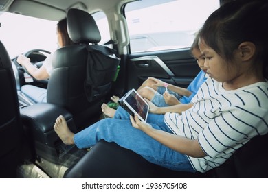 Two Asian Child Girls Sitting On Backseat And Watching Cartoon In Tablet Together While Traveling In The Car With Fun. Childhood And Family Lifestyles In Car Concept.