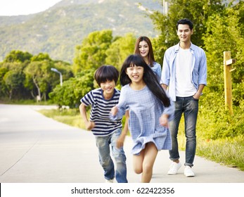 two asian children running in park while their parents watching affectionately.
