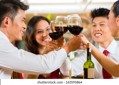 Two Asian Chinese Couples Or Friends Or Business People Toasting During Dinner Or Lunch In A Elegant Restaurant With Red Wine Glasses