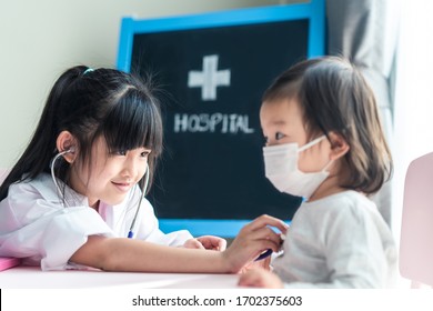 Two Asian Cute Girls Pretend To Be Doctor And Patient. Young Doctor Listening Heartbeat Rate By Using Stethoscope Of Sick Baby Who Wears Mask At Hospital. Doctor Diagnose Disease And Give Some Advice.