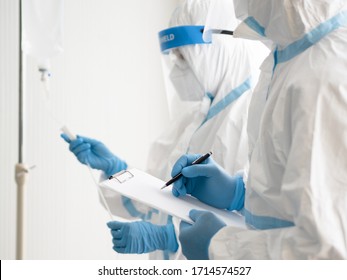 Two Asian Doctor Wear PPE Suit With N95 Mask And Face Shield, Hold Patient Chart And Treat Coronavirus Infected Patient In Negative Pressure Room. Coronavirus, Medical And Covid-19 Concept.