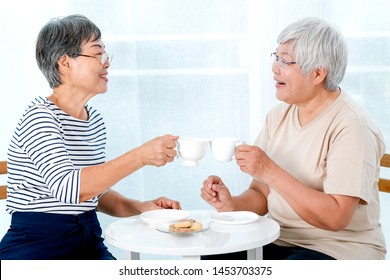 Two Asian Elderly Women Drink Tea Together In The Morning And Also Have Some Cookies, They Are Smile And Talk About Some Stories.