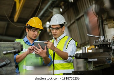 Two Asian Engineering Man Wearing Safety Uniform And Hard Hats Working With Tablet Work Machine Lathe Metal, Heavy Industry Worker Man Concept.