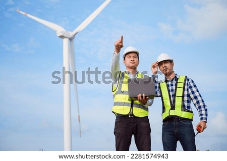 Two asian engineers discussing and checking turbines on wind turbine farm. Renewable energy technology and sustainability.