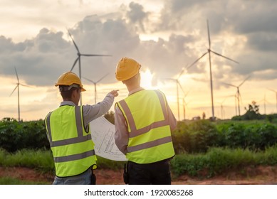 two asian engineers male checking wind turbines during beautiful sunset. Renewable energy technology and sustainability. Alternative energy for future
