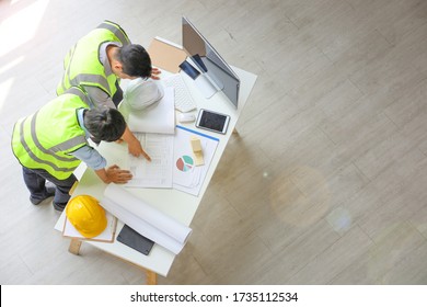 Two Asian Engineers Wearing Safety Equipment While Discussing Over The Future Expanding Business Plan With Blueprint Of The Factory Inside The Warehouse From The Top View Perspective With Copy Space