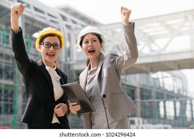 Two Asian female engineer raise their hands up cheering for their victory in a building competition. Their smile to show their happiness. On a building site background. - Shutterstock ID 1024296424