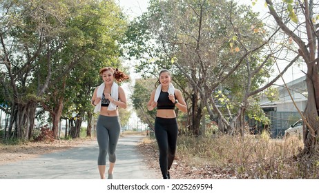 Two Asian Girl Friends In Sportswear Jogging Outdoor Together In The Morning. Happy Woman Running And Talking. Exercise Buddy And Healthy Lifestyle Concept