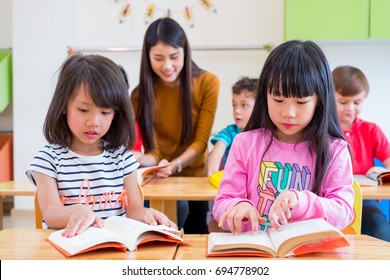 Two Asian Girl Kid Reading Book In Classroom And While Teacher Teach Friends Beside Them,kindergarten Education