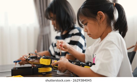 Two Asian girls working together on robotics project at home. Promoting STEM education, teamwork, coding, and problem-solving through hands-on engineering and creative learning.