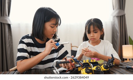 Two Asian girls working together on robotics project at home. Promoting STEM education, teamwork, coding, and problem-solving through hands-on engineering and creative learning.