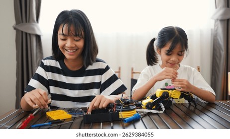 Two Asian girls working together on robotics project at home. Promoting STEM education, teamwork, coding, and problem-solving through hands-on engineering and creative learning.