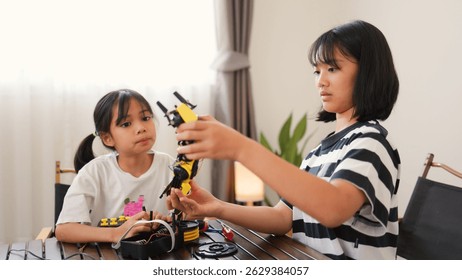 Two Asian girls working together on robotics project at home. Promoting STEM education, teamwork, coding, and problem-solving through hands-on engineering and creative learning.