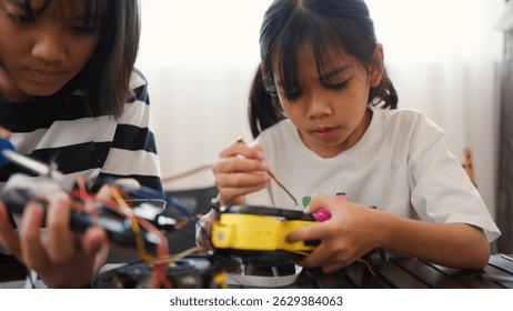 Two Asian girls working together on robotics project at home. Promoting STEM education, teamwork, coding, and problem-solving through hands-on engineering and creative learning.