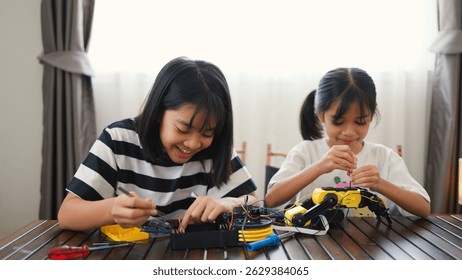 Two Asian girls working together on robotics project at home. Promoting STEM education, teamwork, coding, and problem-solving through hands-on engineering and creative learning.