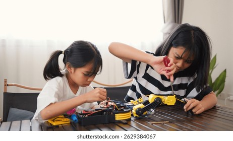 Two Asian girls working together on robotics project at home. Promoting STEM education, teamwork, coding, and problem-solving through hands-on engineering and creative learning.