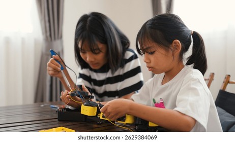 Two Asian girls working together on robotics project at home. Promoting STEM education, teamwork, coding, and problem-solving through hands-on engineering and creative learning.