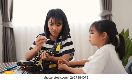 Two Asian girls working together on robotics project at home. Promoting STEM education, teamwork, coding, and problem-solving through hands-on engineering and creative learning.