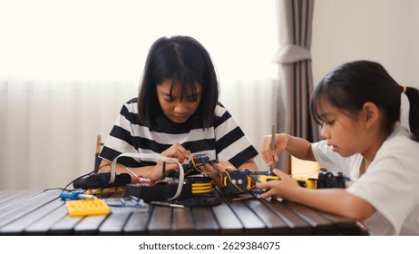Two Asian girls working together on robotics project at home. Promoting STEM education, teamwork, coding, and problem-solving through hands-on engineering and creative learning.