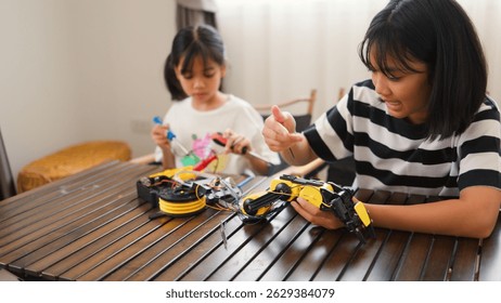 Two Asian girls working together on robotics project at home. Promoting STEM education, teamwork, coding, and problem-solving through hands-on engineering and creative learning.