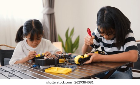 Two Asian girls working together on robotics project at home. Promoting STEM education, teamwork, coding, and problem-solving through hands-on engineering and creative learning.