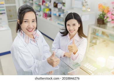 Two Asian Healthcare Worker Show Thumbs Up Sigh With Hands , Unity And Teamwork, On White Background, Happiness Organization, Asian Pharmacist In Drugstore