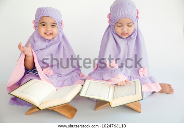 Two Asian little cute Muslim girl reading Quran Holy Book Isolated on White Background