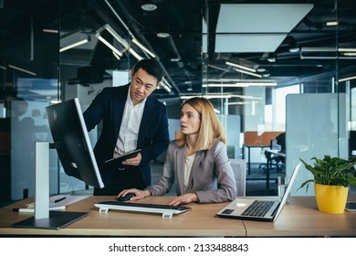 Two Asian male and female colleagues in a modern office, a woman shows the work done on the monitor, consults and discusses