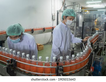 Two Asian Male Workers In Uniform Wearing A Hairnet And Protective Mask Working At Production Line Together In Beverage Factory