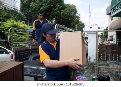 Two Asian Movers In Navy And Orange Uniform Loading Furniture In Truck.