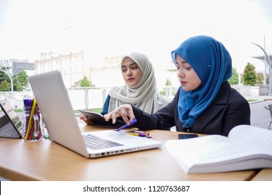 Two asian muslim businesswomen having a business strategy meeting at a cafe using tablet and a laptop. Business team meeting brainstorming working concept.