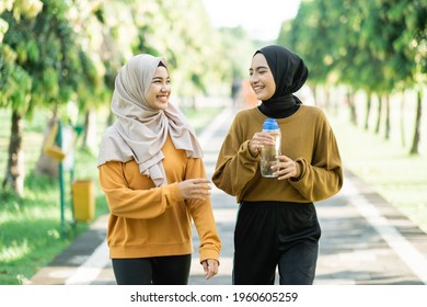 two asian muslim girls enjoy do outdoor sports together while chatting and holding drinking water with a bottle in the park field