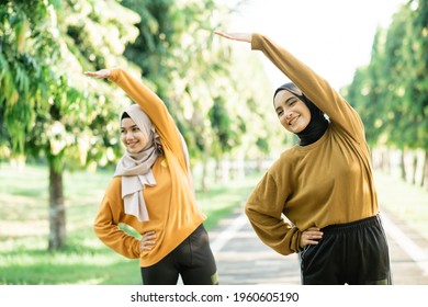 Two asian Muslim girls in headscarves stretch their muscles by raising their hands to exercise outside the room at the park - Powered by Shutterstock