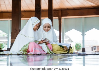 two Asian Muslim girls reading and studying the holy book of the Al-Quran together sitting on the floor