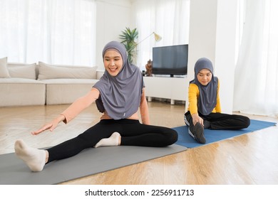 Two Asian muslim women in hijab practicing yoga on mat at home. Smiling muslim women exercising on floor in living room - Shutterstock ID 2256911713