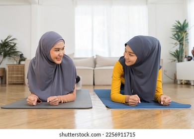Two Asian muslim women in hijab practicing yoga on mat at home. Smiling muslim women exercising on floor in living room - Shutterstock ID 2256911715
