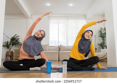 Two Asian muslim women in hijab practicing yoga on mat at home. Smiling muslim women exercising on floor in living room - Shutterstock ID 2256911717