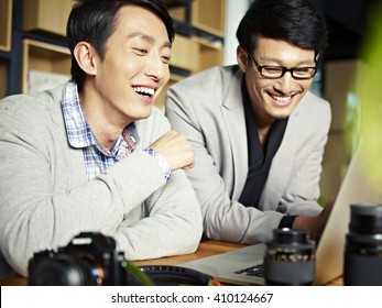 two asian photographers working together selecting images using laptop computer, happy and laughing. - Powered by Shutterstock