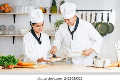 Two Asian professional couple chef wearing white uniform and hat, helping for preparing ingredients for healthy meal, cooking in kitchen together, smiling with happiness and confidence. Food Concept - Powered by Shutterstock