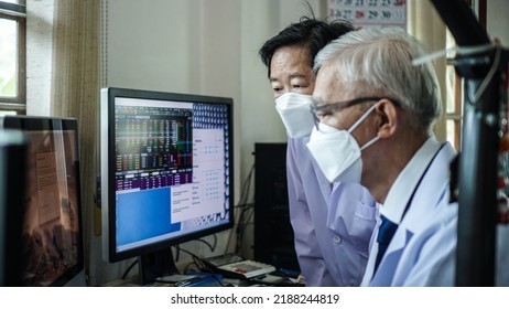 Two Asian Senior Doctor Health Care Technician Looking At Patient Information And Discussing Computer Screen