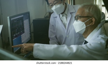 Two Asian Senior Doctor Health Care Technician Looking At Patient Information And Discussing Computer Screen