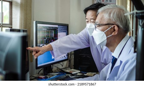 Two Asian Senior Doctor Health Care Technician Looking At Patient Information And Discussing Computer Screen