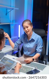 Dois engenheiros de software asiáticos colaboram à noite em escritórios modernos, escrevendo algoritmos de aprendizado de máquina e depurando código de inteligência artificial em vários monitores no fluxo de trabalho de desenvolvimento tecnológico de IA.