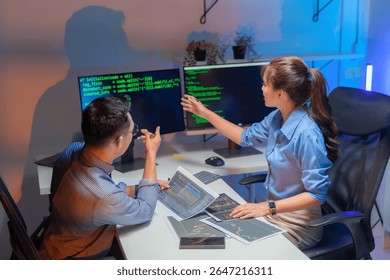 Dois engenheiros de software asiáticos colaboram à noite em escritórios modernos, escrevendo algoritmos de aprendizado de máquina e depurando código de inteligência artificial em vários monitores no fluxo de trabalho de desenvolvimento tecnológico de IA.