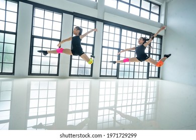 Two Asian teenage girls dance high-jump ballets together beautifully in a comtemporary performance in a studio class. 