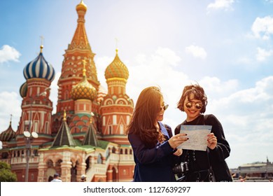 Two Asian Traveler Girls Are Looking At The Map With Smiley Face In Front Of St.Basil's Cathedral On Red Square In Moscow. Famous Travel Landmark In Europe Concept.